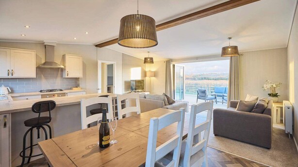 A modern kitchen with white cabinets, a wooden dining table, and a view of the outdoors. - Host & Stay | Hazelwood Deluxe Lodge (Low Gate)