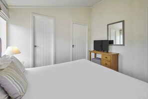 A bedroom with a bed, a bedside table with a television, a lamp, and two doors.