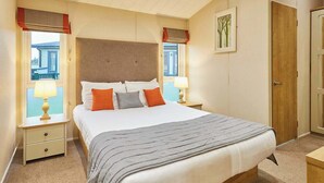 Une chambre à coucher bien rangée, avec un lit, des lampes de chevet, une table de chevet, une porte et une fenêtre donnant sur un beau paysage.