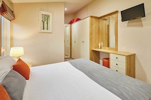 Une chambre d’hôtel comprenant un lit, un bureau, une armoire, un miroir et un téléviseur.