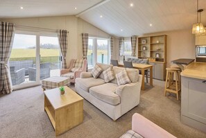 A cozy living room with a sofa, armchairs, a coffee table, and a dining area with a table and chairs. There is a bookshelf and a kitchen area with a counter and stools. - Host & Stay | Portland Three (Low Gate)