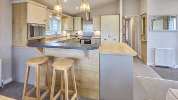 A modern kitchen with a central island, bar stools, pendant lighting, and a view of the living area.