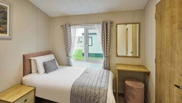 A bedroom with a bed, bedside table, and a small stool. There is a window with curtains and a view of the outside.