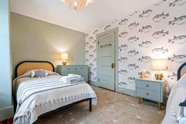 A bedroom with a bed, two bedside tables, a nightstand, a door, and a wall with fish patterns.