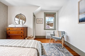 Une chambre à coucher comprenant un lit, une commode, une chaise, une fenêtre et des œuvres d’art.