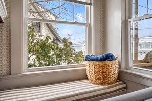A window seat with a woven basket and a striped cushion. - Steps to Beach & Downtown OGT | Porch w Ocean View (Ogunquit)