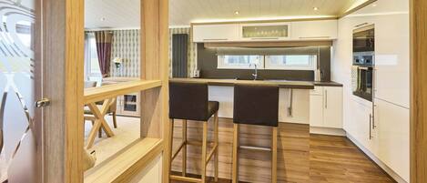 Una cocina moderna con piso de madera, muebles blancos y una barra con taburetes.