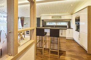 A modern kitchen with wooden flooring, white cabinetry, and a bar area with stools.