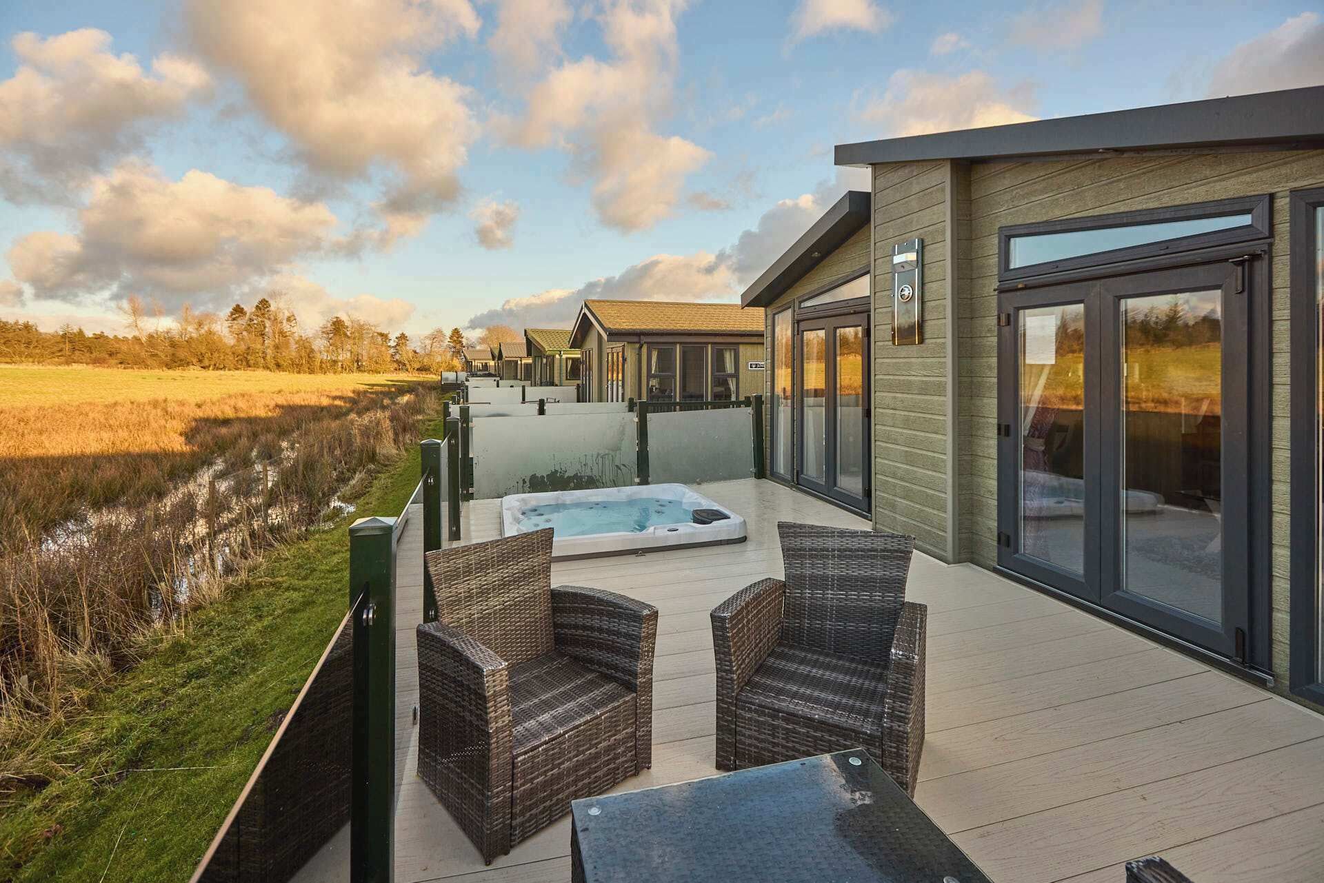 A deck with wicker furniture and a hot tub, overlooking a natural landscape.