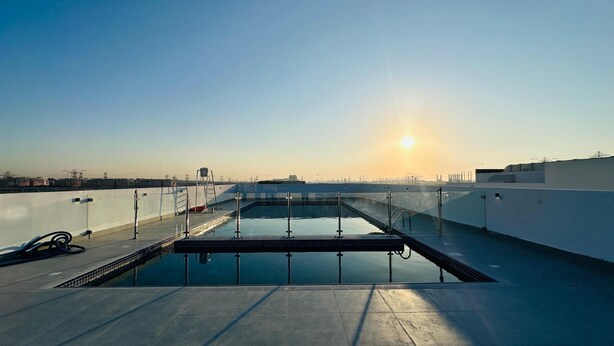 Una piscina en la azotea con vistas despejadas al atardecer, rodeada por un edificio blanco y líneas eléctricas.