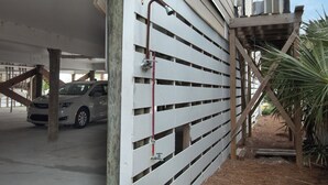 A parking garage with a white fence, a car, and a wooden structure. - Oceanfront 30+ day rental! (Folly Beach)