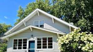 A single-story house with a front porch, a blue door, and a small front yard with various plants and a tree with white flowers. - Pleasant Stay in Pella (Pella)