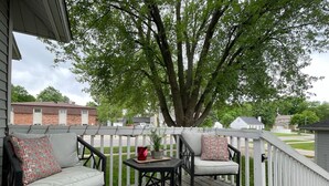 A covered outdoor deck with two cushioned chairs, a small table, and a potted plant. - Pleasant Stay in Pella (Pella)