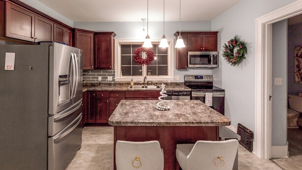 A kitchen with a granite countertop, stainless steel appliances, wooden cabinets, and a central island with two chairs. - Pleasant Stay in Pella (Pella)