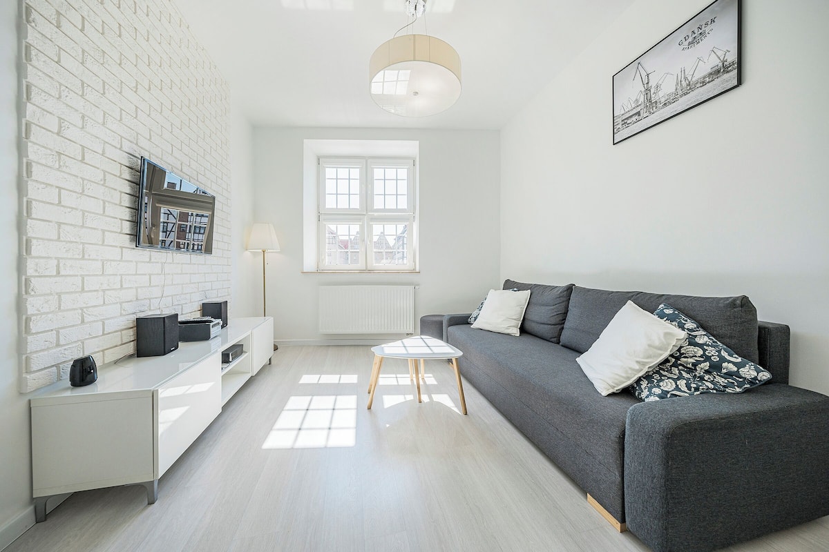 A modern living room with a white brick wall, a grey sofa, a small white table, and a framed picture on the wall.