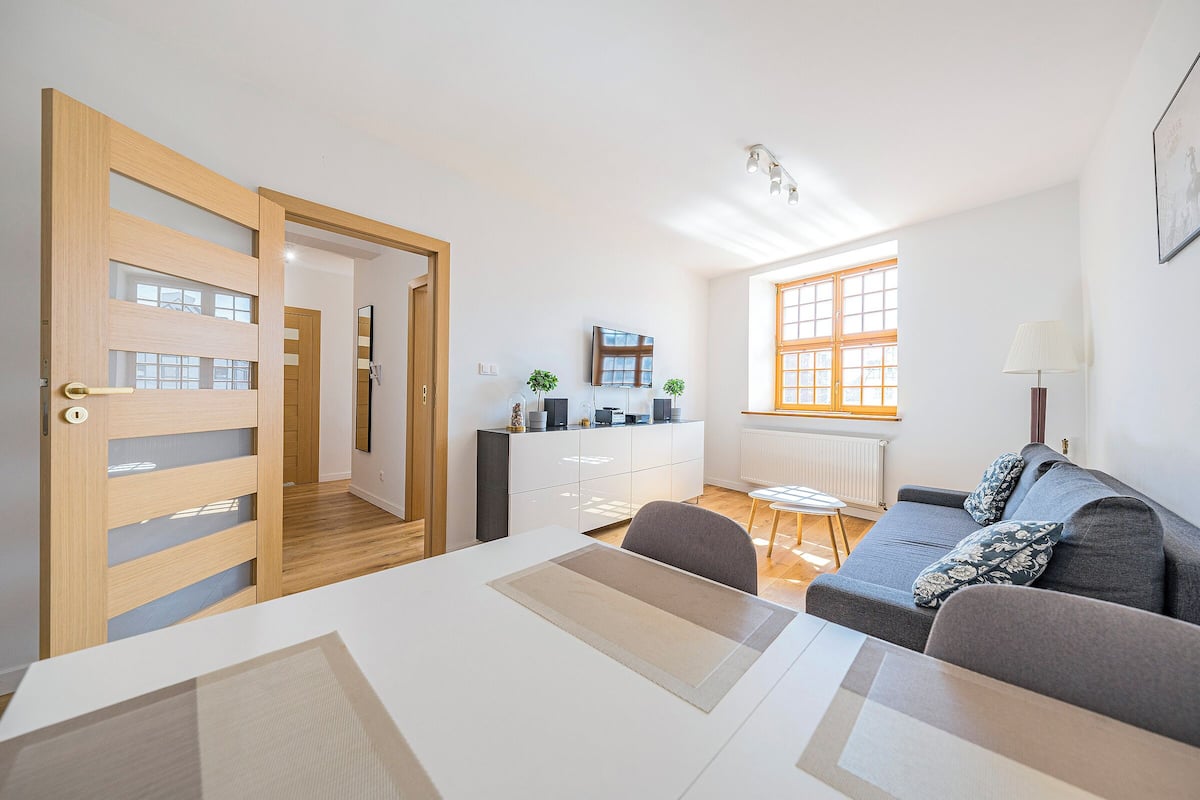 A modern living room with a sofa, a dining table, and a kitchen area in the background.