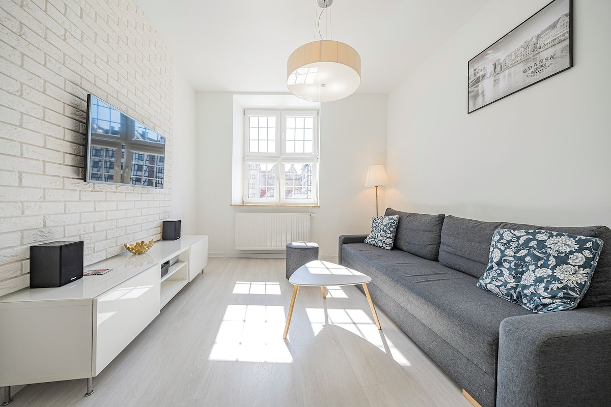A modern living room with a white brick wall, a grey sofa, a small white table, and a framed picture of Copenhagen.