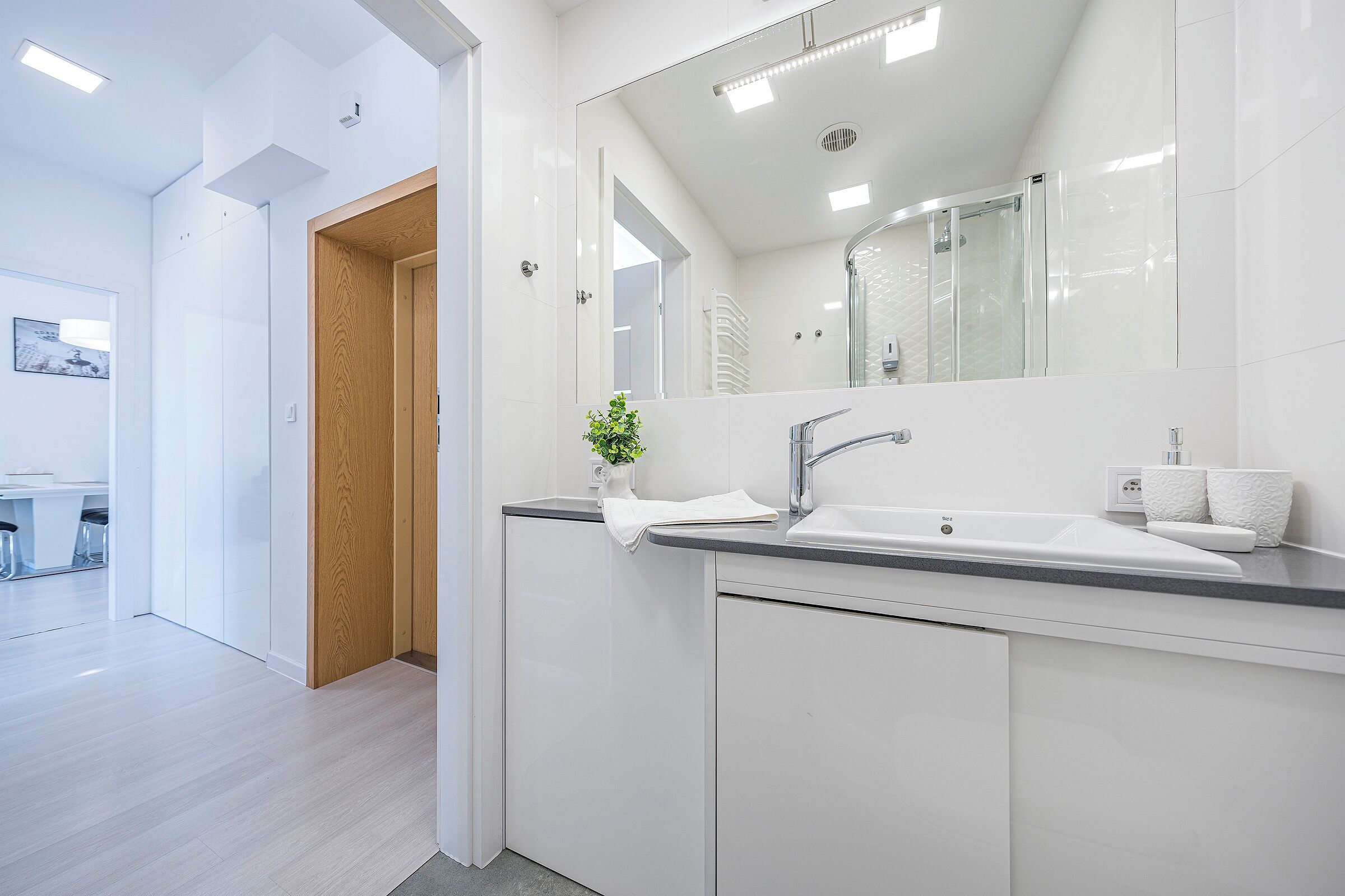 A modern bathroom with a white sink, mirror, and wooden door.