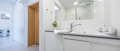 A modern bathroom with a white sink, mirror, and wooden door.