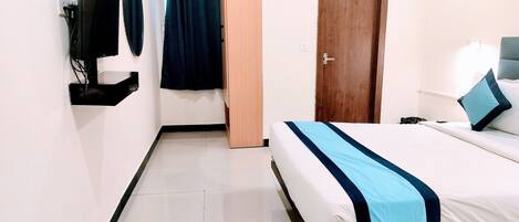 A hotel room with a bed, a TV mounted on the wall, a door, and a curtain.