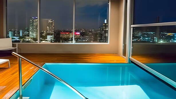 Une piscine intérieure moderne dotée d’une balustrade en verre, d’un plancher en bois et offrant une vue sur la ville grâce à de grandes fenêtres.