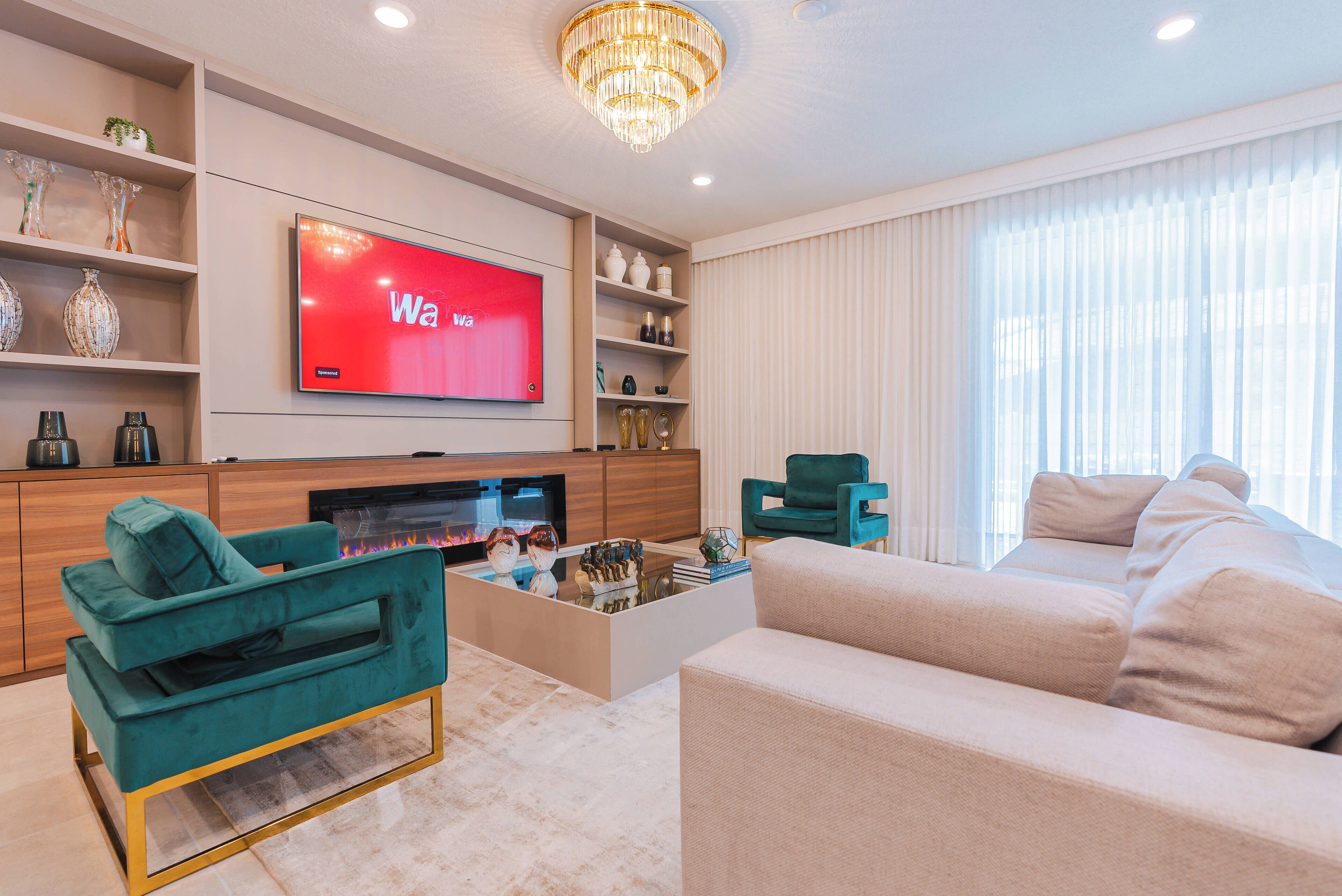 Una sala de estar moderna con un televisor de pantalla plana, sofás verde azulado y beige, una mesa de centro y objetos decorativos en estanterías.
