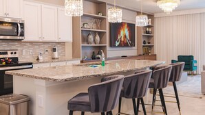 A modern kitchen with a large island, bar stools, a microwave, and a chandelier.