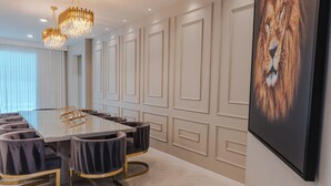 A conference room with a glass table, six upholstered chairs, a chandelier, and a large framed picture of a lion on the wall.