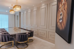 Uma sala de conferências com uma mesa de vidro, seis cadeiras estofadas, um candelabro e um quadro grande de um leão na parede.
