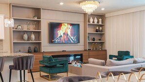 A modern living room with a flat-screen TV, teal and grey sofas, a coffee table, and a chandelier.