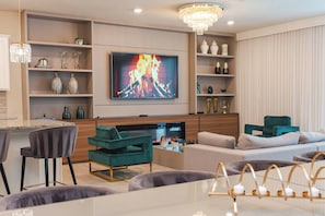 Uma sala de estar moderna com televisão de tela plana, sofás verde-água e cinza, uma mesa de centro e um lustre.