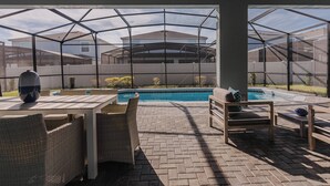 A covered outdoor area with a pool, wicker furniture, and a view of neighboring houses.