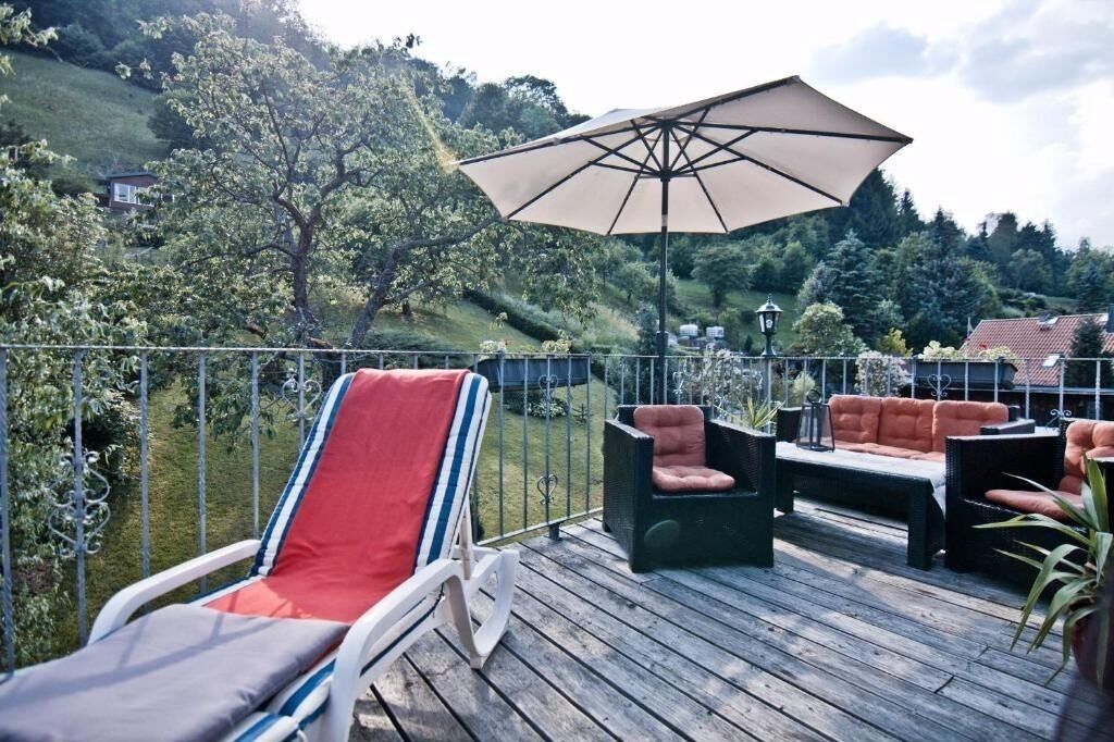 A wooden deck with outdoor furniture, including a lounge chair and a sofa, and a large umbrella providing shade.