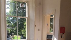 A dining room with a long wooden table, chairs, a bowl of fruit, and a window with a view of greenery outside. - Traditional Victorian Edinburgh Flat Central Location, Bright and Airy (Edinburgh)