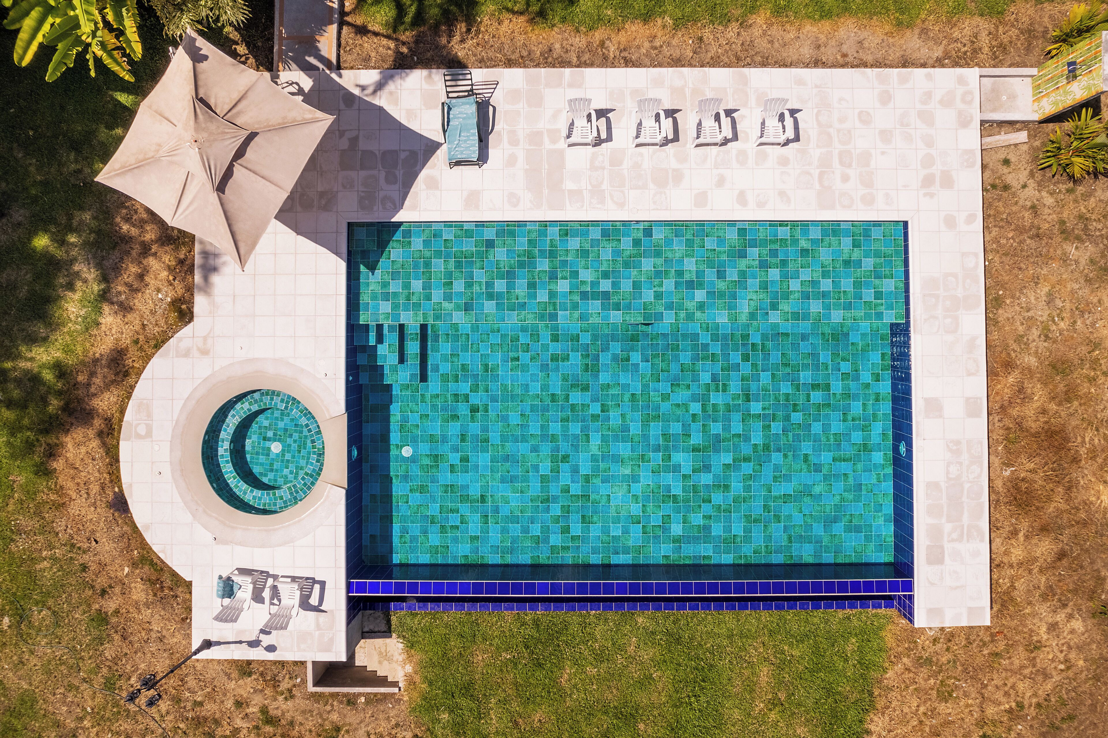 An aerial view of a swimming pool with a tiled deck, lounge chairs, and a circular hot tub area.