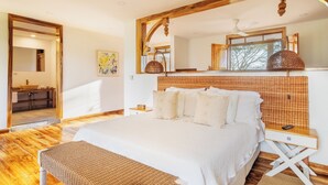 A bedroom with a large bed, wooden floor, a small bedside table, a nightstand, a mirror, and a window with a view of trees. - Casa de Campo el Edén (Armenia)