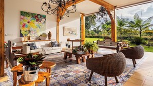 A spacious living area with a large window, wooden ceiling beams, a chandelier, and a variety of seating and decorative items. - Casa de Campo el Edén (Armenia)