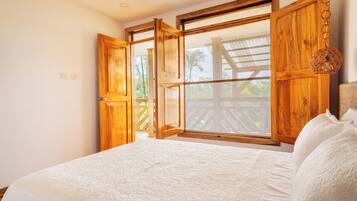 Une chambre avec un grand lit, une armoire en bois et une fenêtre donnant sur une terrasse en bois et des palmiers.