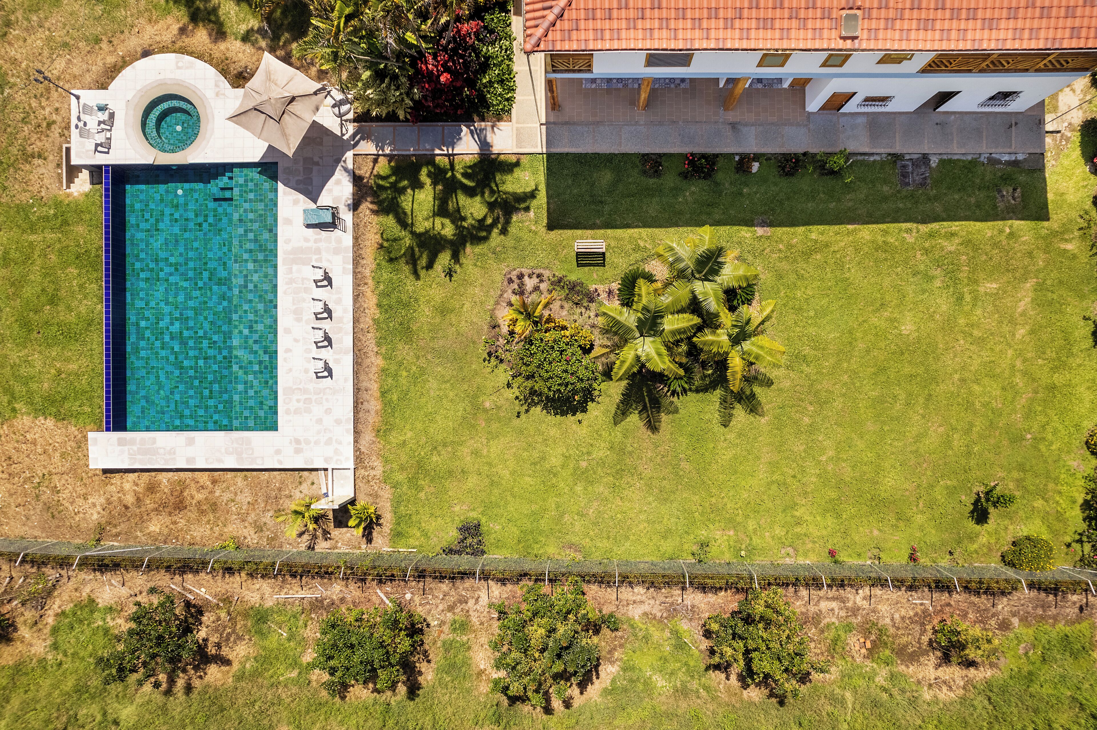 An aerial view of a property with a swimming pool, a covered patio, and a well-maintained lawn.