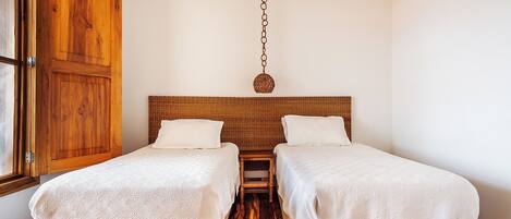 A room with two single beds, a wooden wardrobe, and a hanging light fixture.