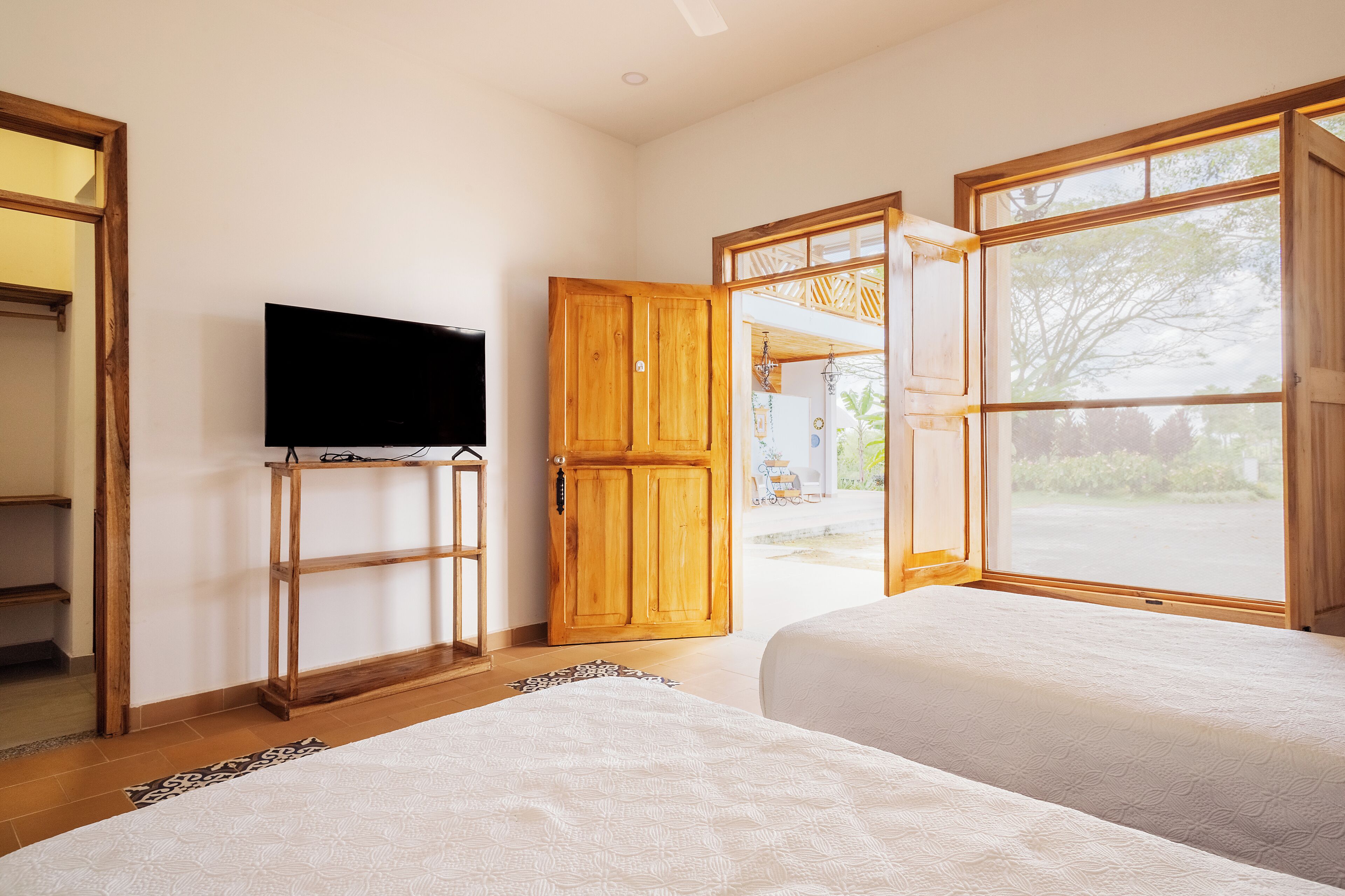 A bedroom with two beds, a television, and wooden doors leading to an outdoor area.