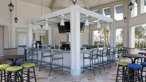 An outdoor bar area with multiple seating options, including bar stools and tables, and a counter with a television screen. - 5BR house with game room near Disney (Kissimmee)