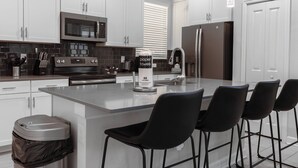 A modern kitchen with white cabinets, stainless steel appliances, and a central island with bar stools. - 5BR house with game room near Disney (Kissimmee)