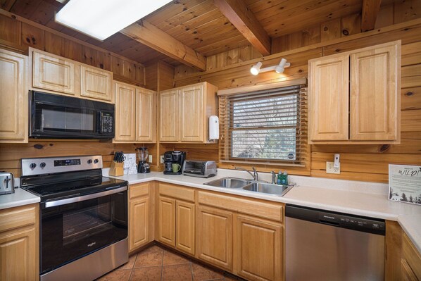 A kitchen with wooden cabinets, a stainless steel stove, a microwave, a dishwasher, and a window with blinds.