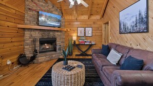 A cozy log cabin interior with a fireplace, leather sofa, and a mounted television.