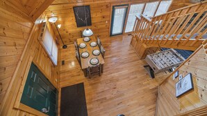 A wooden cabin interior with a dining area, a staircase, and a view of the outdoors.