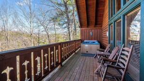 A wooden deck with a hot tub and wooden chairs, overlooking a forested area.