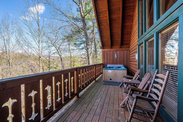 Una terraza de madera con un jacuzzi y sillas de madera, con vista a una zona boscosa.