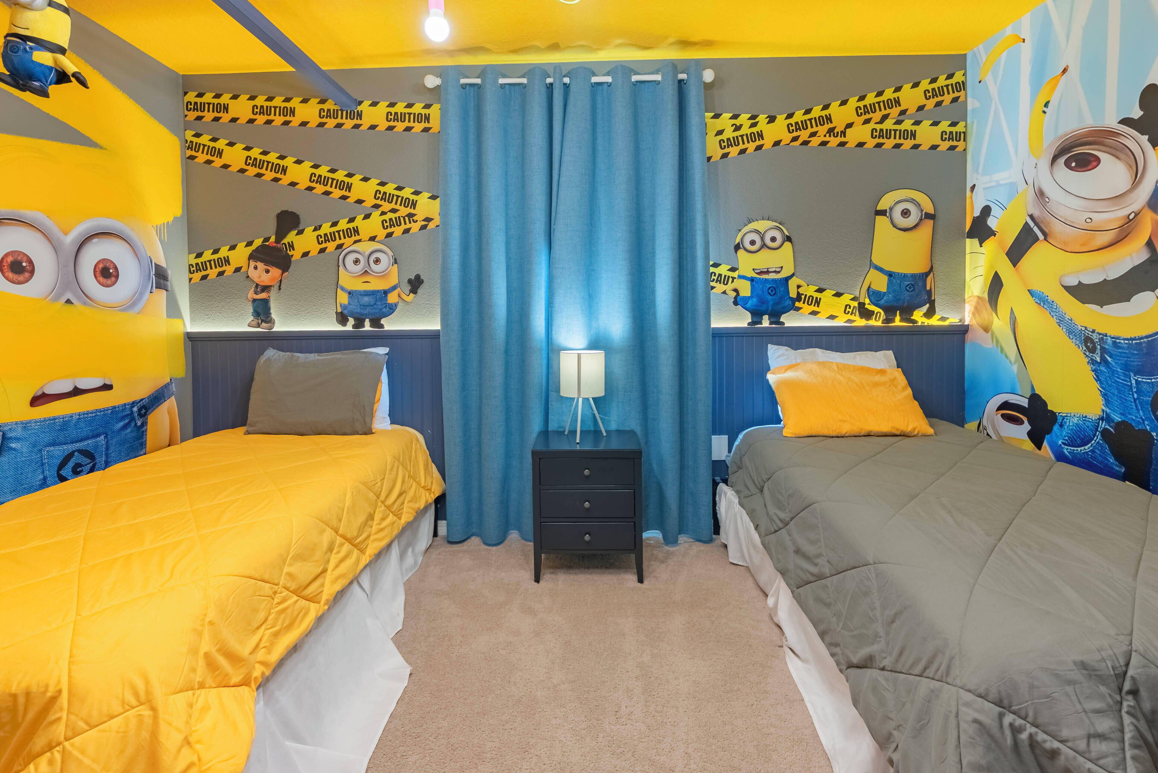Un dormitorio con dos camas, una mesita de noche y un espejo. Las paredes están decoradas con papel tapiz con motivos de los Minions.