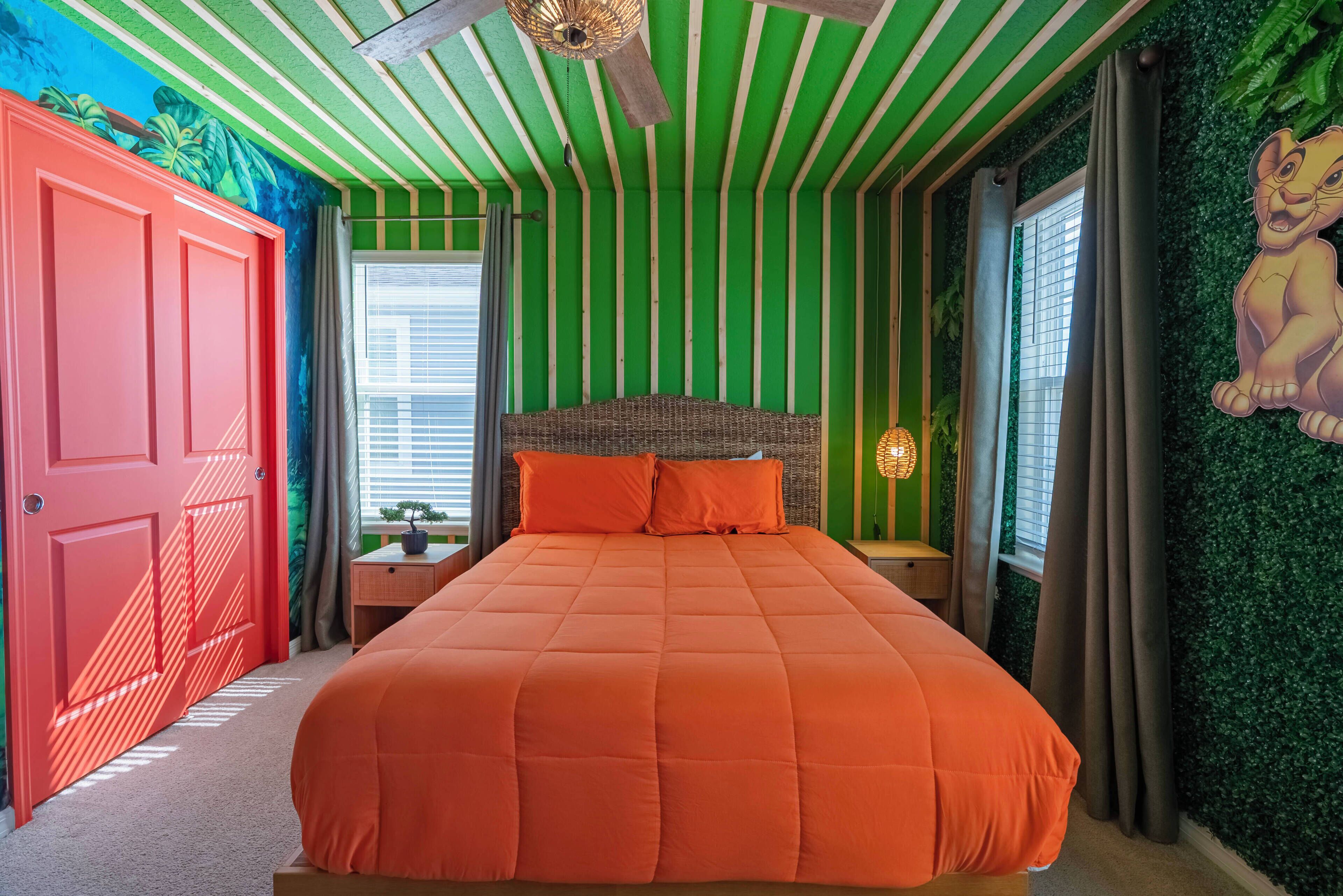 A bedroom with a large bed, green striped walls, a red door, and a window with curtains.